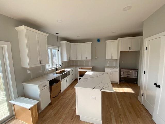 kitchen featuring a sink, white cabinetry, light wood-style floors, hanging light fixtures, and a center island