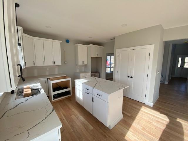 kitchen with light wood finished floors, white cabinetry, a kitchen island, and light stone counters