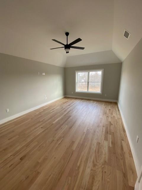 empty room featuring a ceiling fan, light wood-type flooring, vaulted ceiling, and baseboards