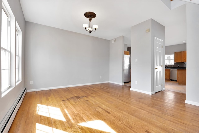 empty room with a chandelier, a baseboard radiator, light wood-style flooring, visible vents, and baseboards