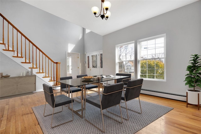 dining area featuring light wood-type flooring, stairway, a baseboard radiator, and an inviting chandelier