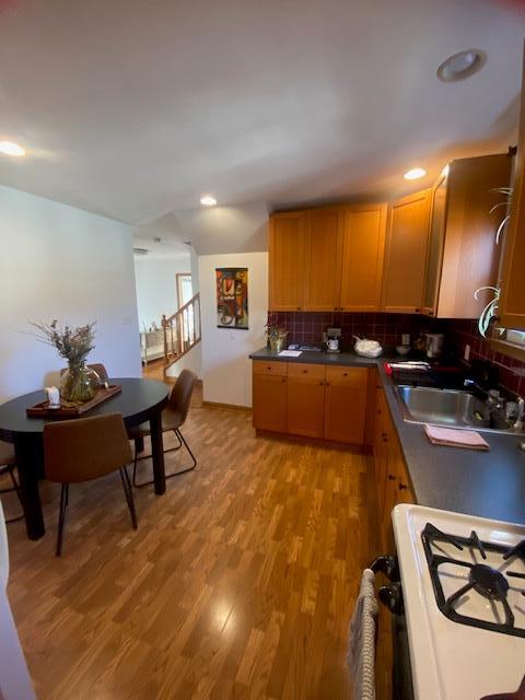 kitchen with decorative backsplash, dark countertops, light wood-type flooring, and a sink