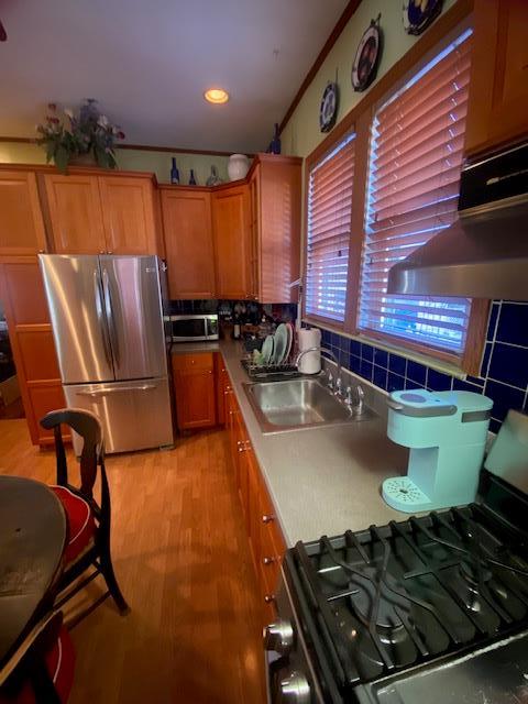 kitchen with light wood-type flooring, brown cabinets, a sink, tasteful backsplash, and appliances with stainless steel finishes