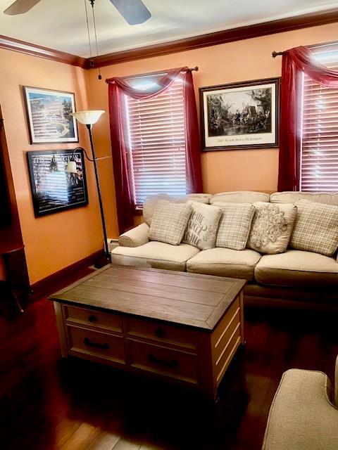 living room featuring baseboards, ceiling fan, dark wood finished floors, ornamental molding, and plenty of natural light