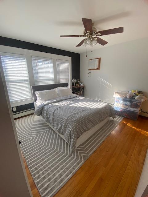 bedroom with baseboard heating, ceiling fan, and wood finished floors