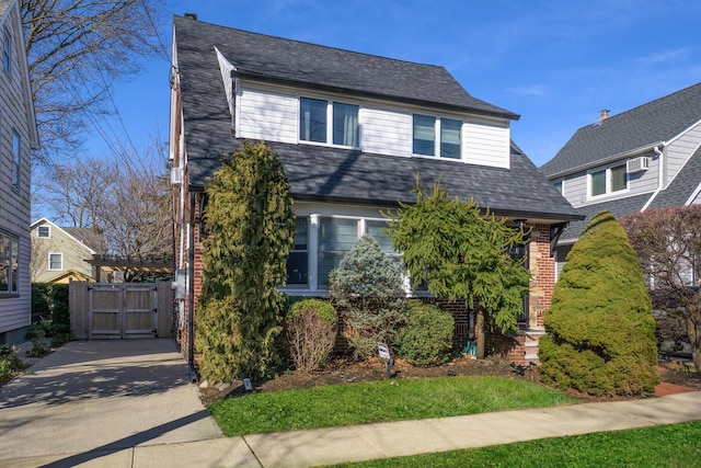 dutch colonial with brick siding, a shingled roof, and a gate