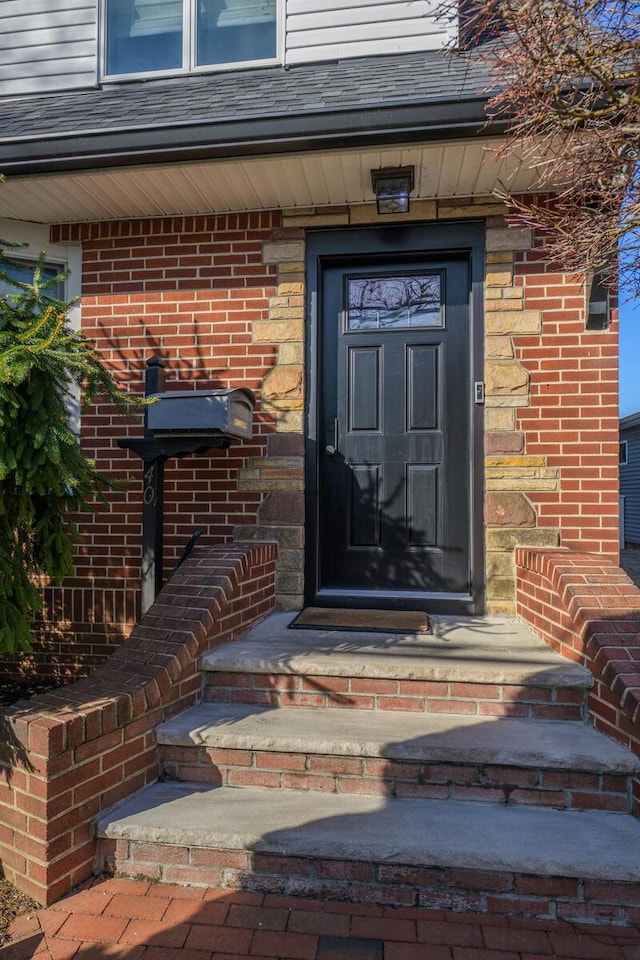 doorway to property with brick siding and roof with shingles