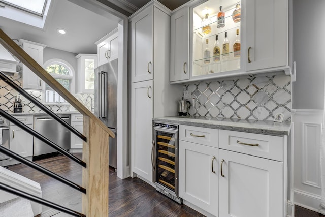 bar featuring beverage cooler, dark wood finished floors, a bar, appliances with stainless steel finishes, and backsplash