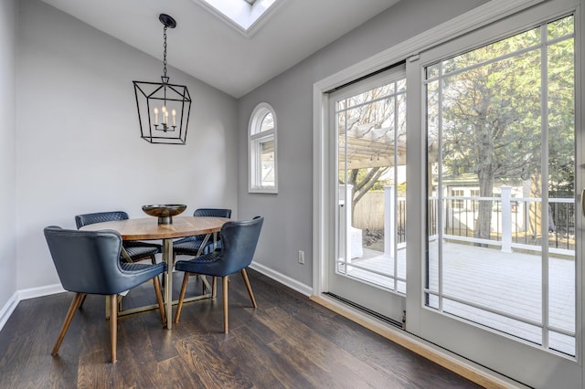 dining room featuring dark wood-style floors, a notable chandelier, vaulted ceiling with skylight, and baseboards