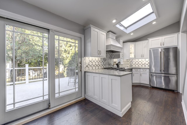 kitchen with vaulted ceiling with skylight, appliances with stainless steel finishes, a healthy amount of sunlight, and custom range hood