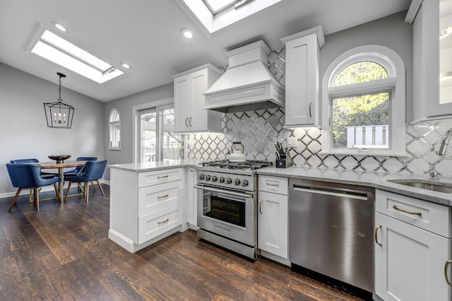 kitchen featuring light stone countertops, lofted ceiling, custom range hood, stainless steel appliances, and a sink