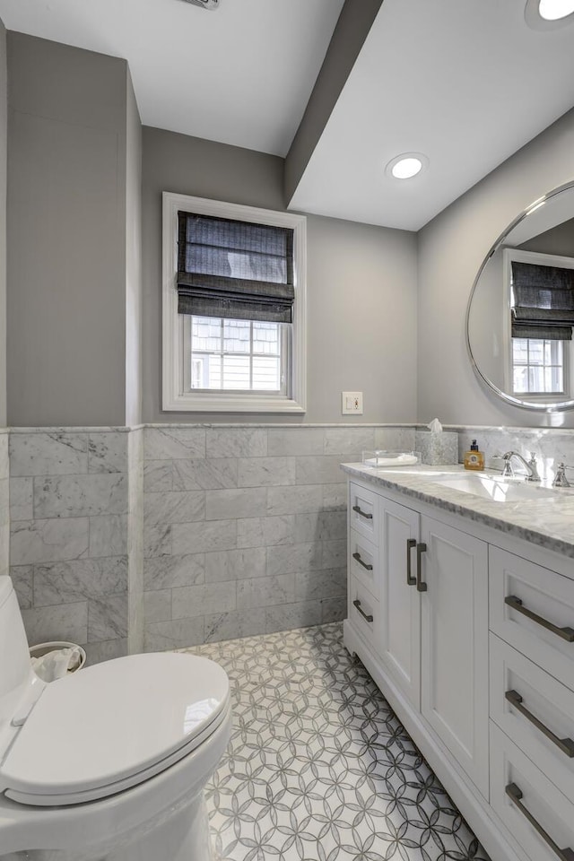 bathroom featuring tile walls, toilet, a healthy amount of sunlight, and a wainscoted wall