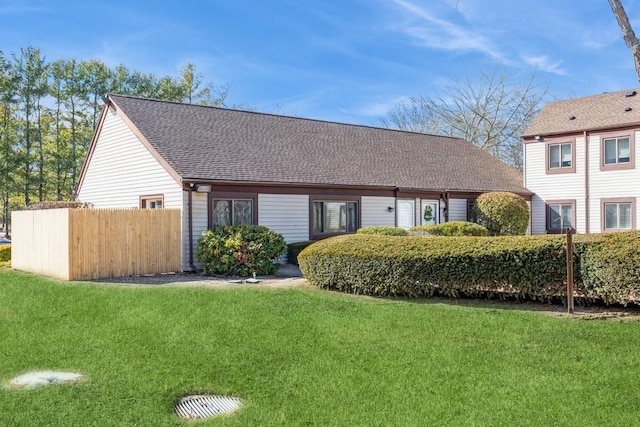 rear view of property featuring roof with shingles, a yard, and fence