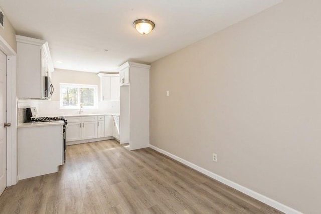 kitchen featuring baseboards, white cabinets, light wood-style floors, stainless steel microwave, and range with gas cooktop