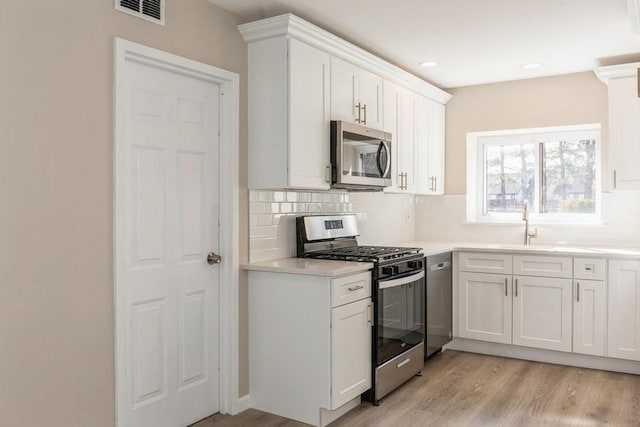 kitchen with light wood-style flooring, stainless steel appliances, visible vents, white cabinetry, and backsplash