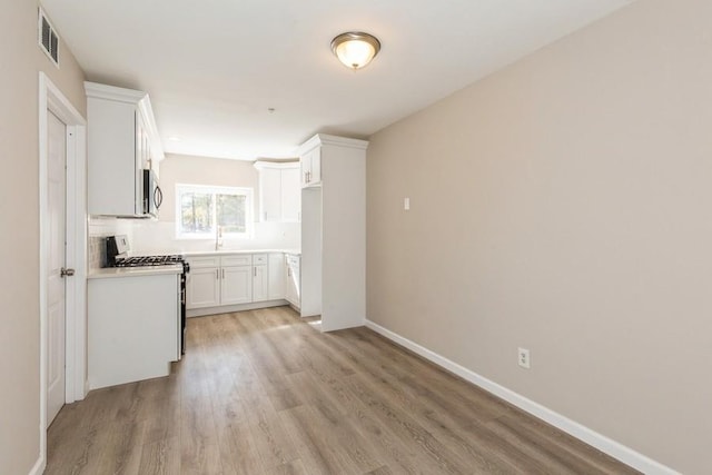 kitchen featuring stainless steel appliances, visible vents, white cabinetry, light wood-type flooring, and decorative backsplash