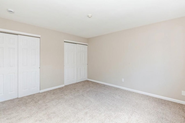 unfurnished bedroom featuring carpet floors, baseboards, and multiple closets