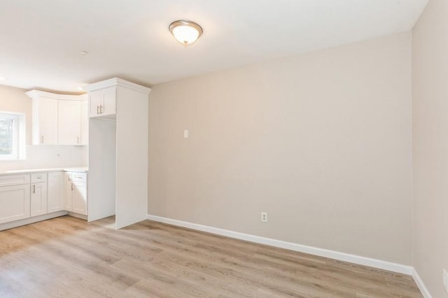 kitchen featuring baseboards, light countertops, white cabinetry, and light wood-style floors