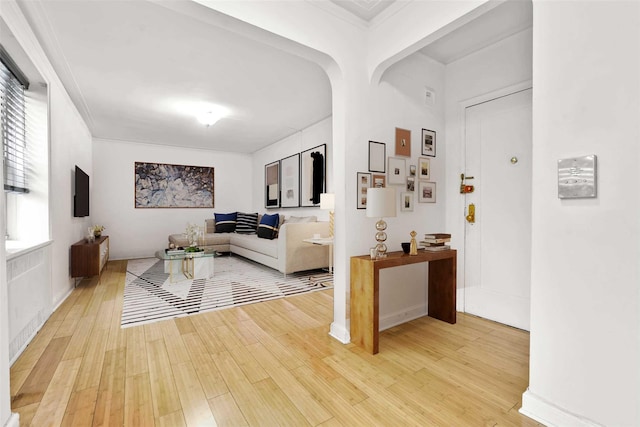 living area featuring arched walkways, ornamental molding, and light wood-type flooring