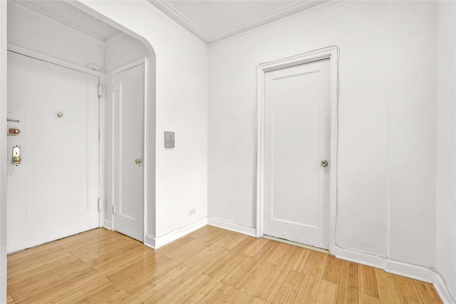 entryway with light wood-style floors, baseboards, arched walkways, and crown molding