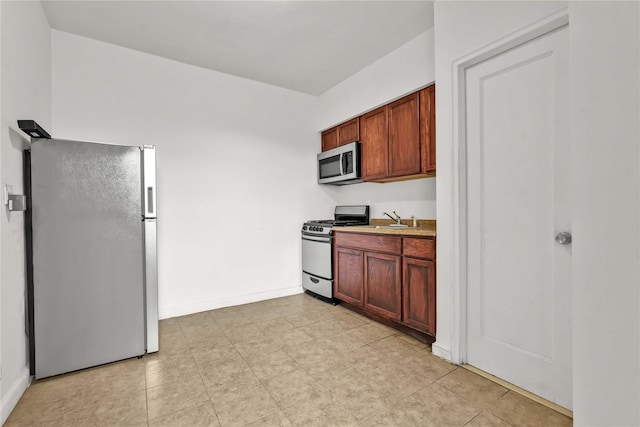 kitchen featuring baseboards, appliances with stainless steel finishes, and a sink