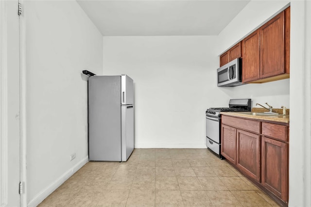 kitchen with light tile patterned floors, baseboards, stainless steel appliances, and light countertops