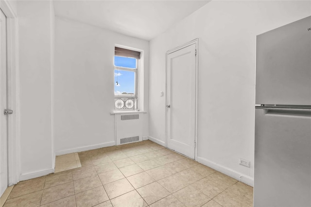 unfurnished bedroom featuring light tile patterned floors, baseboards, freestanding refrigerator, and radiator