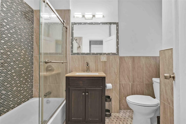 bathroom featuring shower / bath combination with glass door, tile walls, toilet, and vanity