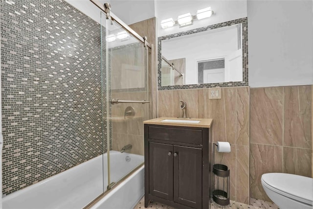 full bathroom with toilet, bath / shower combo with glass door, tile walls, and vanity