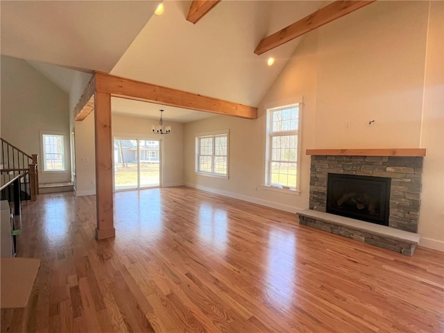 unfurnished living room featuring beam ceiling, stairway, a stone fireplace, wood finished floors, and high vaulted ceiling