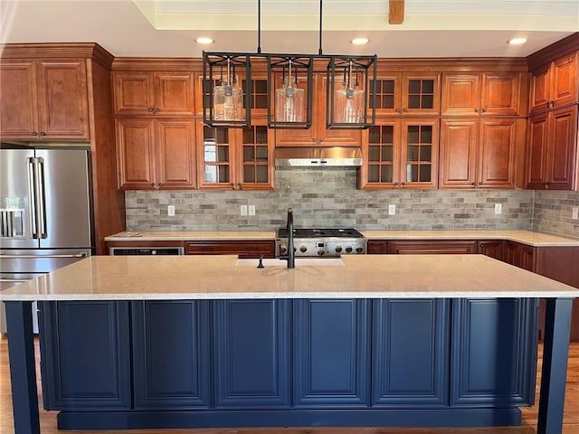 kitchen with under cabinet range hood, backsplash, range, stainless steel fridge with ice dispenser, and an island with sink