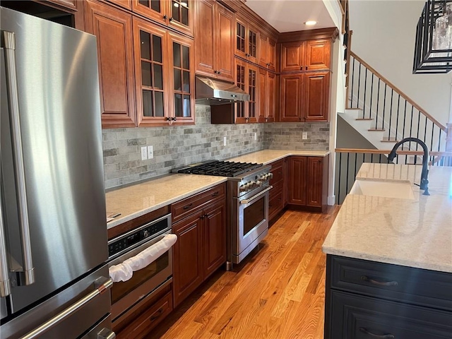 kitchen with premium appliances, light wood-style flooring, backsplash, under cabinet range hood, and a sink