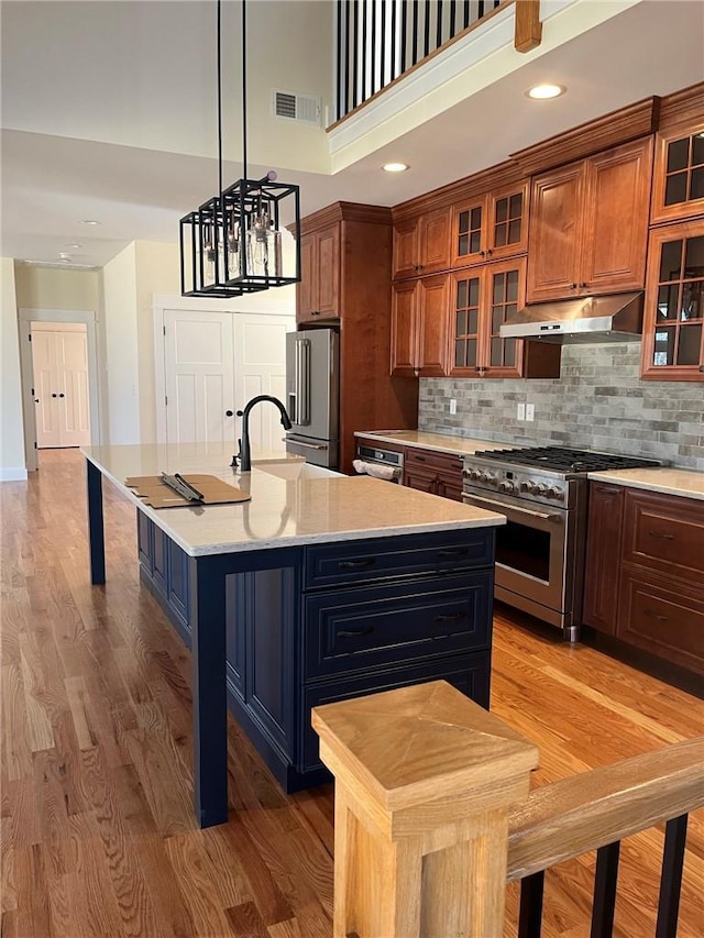 kitchen with light wood finished floors, brown cabinetry, high quality appliances, light countertops, and under cabinet range hood