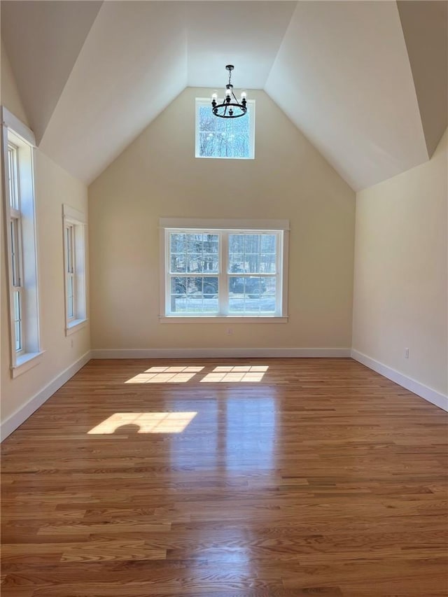 additional living space featuring lofted ceiling, a chandelier, wood finished floors, and baseboards