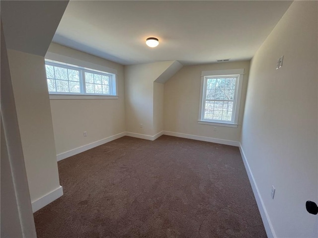 additional living space featuring baseboards, visible vents, dark colored carpet, and a wealth of natural light