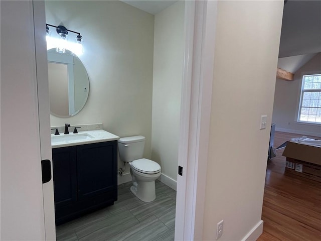 bathroom featuring toilet, wood finished floors, vanity, baseboards, and vaulted ceiling