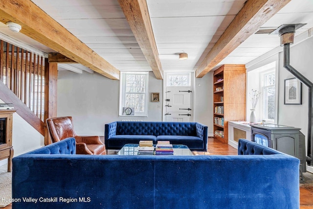 living room with wood finished floors, visible vents, a wood stove, stairs, and beamed ceiling