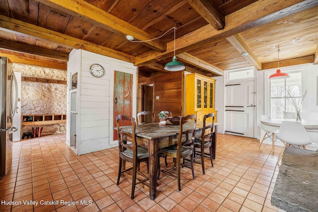 dining room featuring beam ceiling, wooden walls, light tile patterned flooring, and wood ceiling