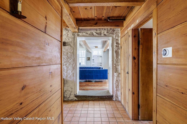 hallway featuring wooden ceiling, beamed ceiling, light tile patterned floors, and wood walls