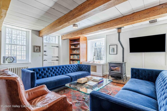 living room featuring radiator, baseboards, beam ceiling, a wood stove, and wood finished floors