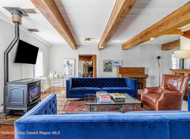 living area with beam ceiling, visible vents, a wood stove, and wood finished floors