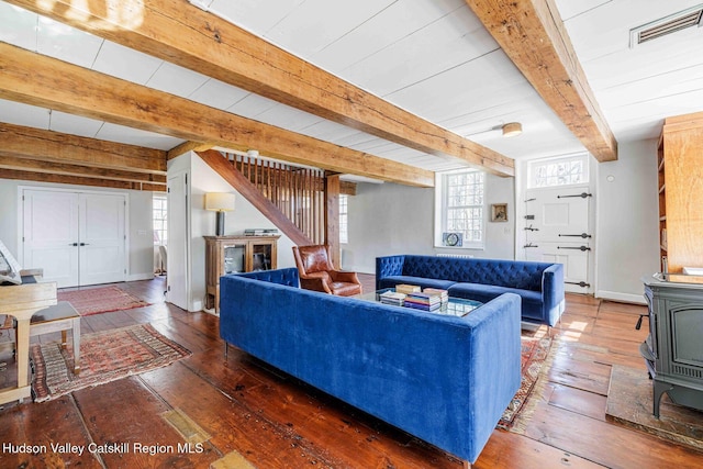 living area featuring beam ceiling, visible vents, a wood stove, and hardwood / wood-style flooring