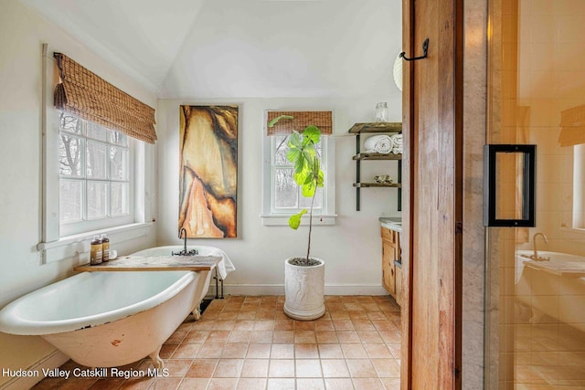 full bath featuring vanity, baseboards, a freestanding bath, tile patterned flooring, and vaulted ceiling