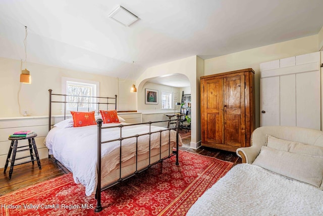 bedroom featuring lofted ceiling, multiple windows, wood finished floors, and arched walkways