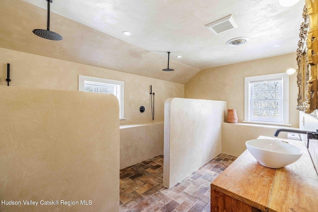 bathroom with vaulted ceiling, visible vents, and walk in shower