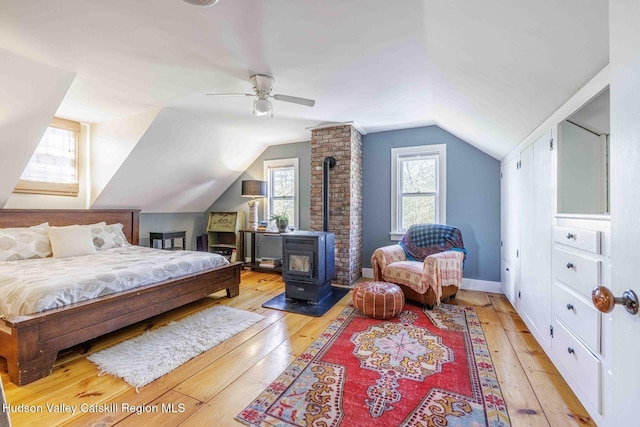 bedroom with ceiling fan, lofted ceiling, light wood-style floors, and a wood stove