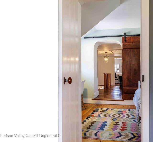 corridor featuring light wood-type flooring, a barn door, and arched walkways