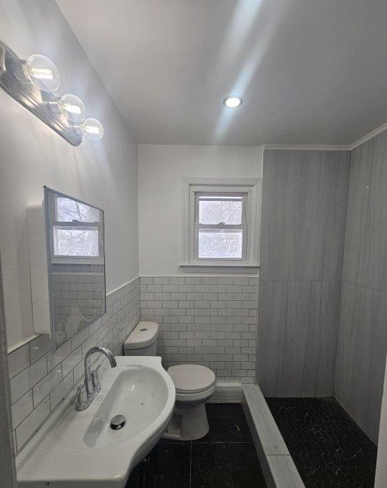 bathroom featuring toilet, a sink, tile walls, tile patterned flooring, and tiled shower