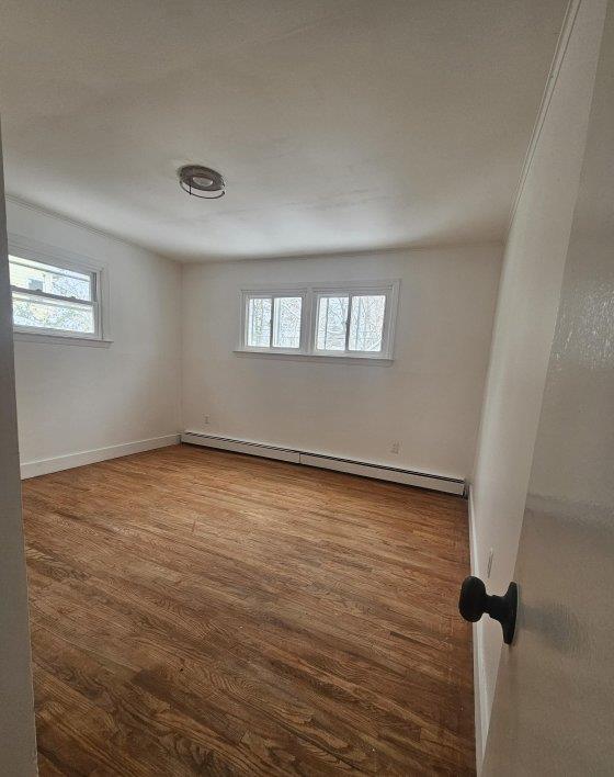 unfurnished room featuring wood finished floors, baseboards, and a baseboard radiator