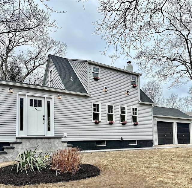 rear view of property with a garage, roof with shingles, and a chimney